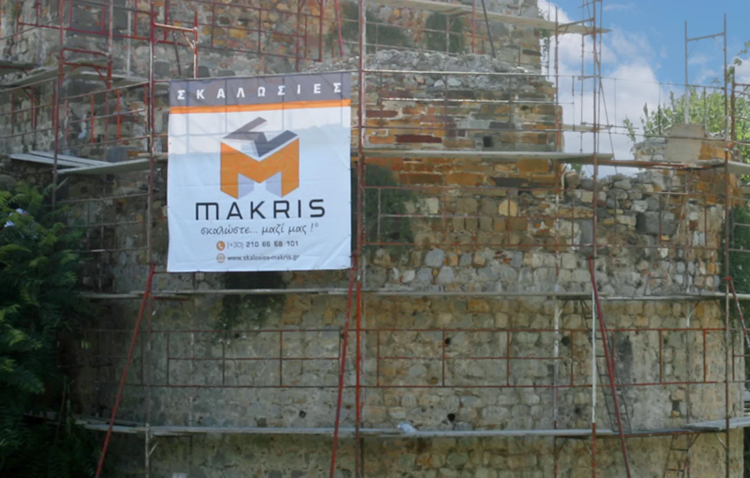 Banner από μουσαμά, στερεωμένος σε σκαλωσιά πάνω σε πέτρινο πύργο, σε εξωτερικό χώρο